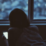 A photo of a woman lying on a bed while using her smartphone for the article "Studies: Health Effects of Blue Light Exposure"