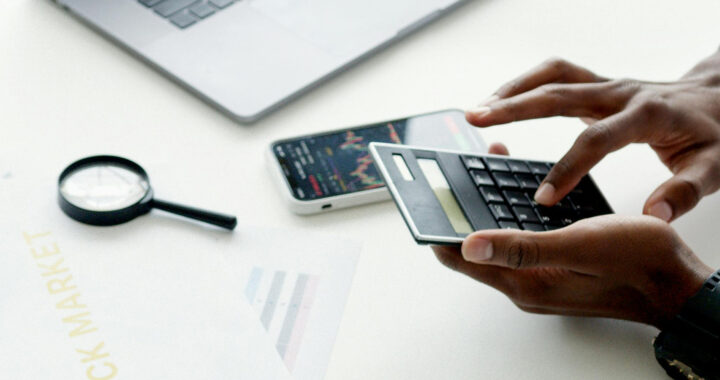 An image of a person's hands using a calculator for the article "Unrealized Capital Gains Tax: Advantages and Disadvantages"