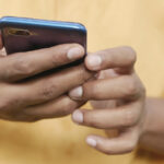 A closeup image of hands of a man holding a smartphone for the article "5G SA vs 5G NSA: What are Standalone and Non-Standalone Modes?"