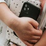 A close-up iphoto of what appears to be a woman carrying her phone, tablet, and newspapers for the article "Psychological Factors Influencing False Information Acceptance"