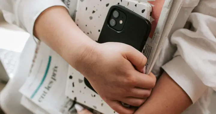 A close-up iphoto of what appears to be a woman carrying her phone, tablet, and newspapers for the article "Psychological Factors Influencing False Information Acceptance"