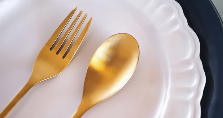 A tight shot of golden spoon and fork on an empty white plate for the article "Study: How Intermittent Fasting Slows Hair Growth"