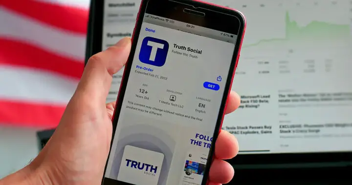 A hand holding a smartphone with an on-screen download prompt for the Truth Social app for the article "The Financial Struggles of Trump Media"