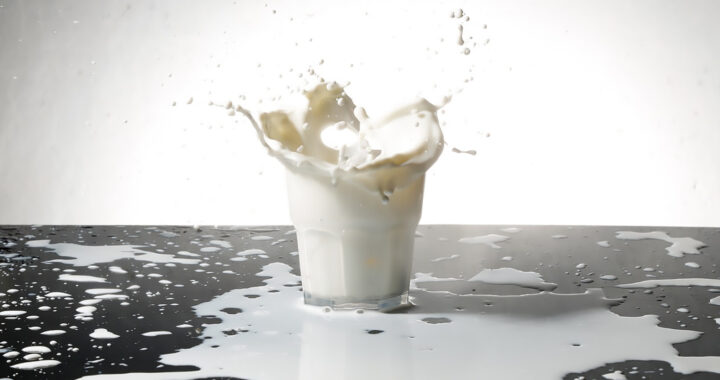 A glass of overflowing milk that spilled on the table for the article "Dangers From Raw Milk Consumption: Common Diseases"